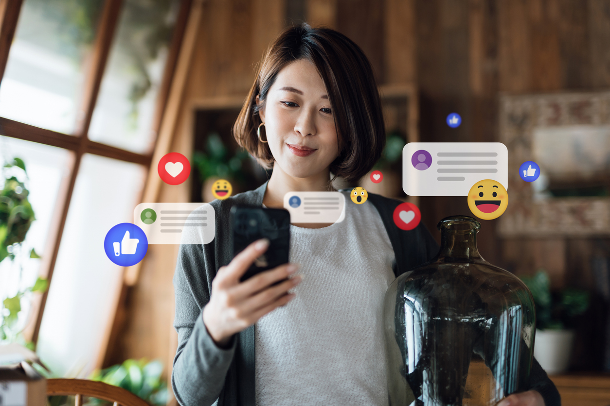 Young Asian woman using smartphone in the living room at home, checking social media on mobile phone. Social media listening is one way to measure brand health.