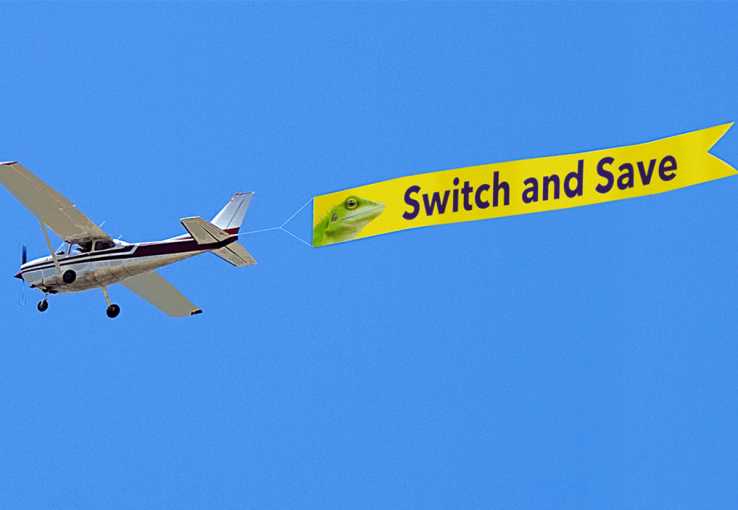 Airplane pulling a yellow "switch and save" advertisement banner behind it in the air.