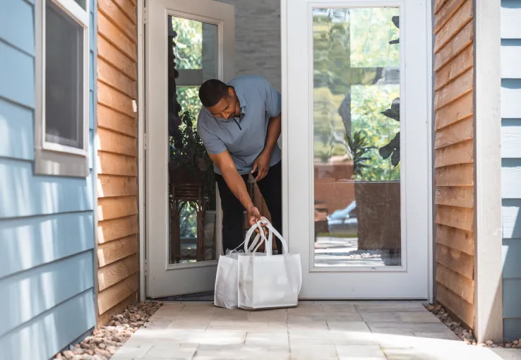 Man retrieves groceries from porch after contactless delivery